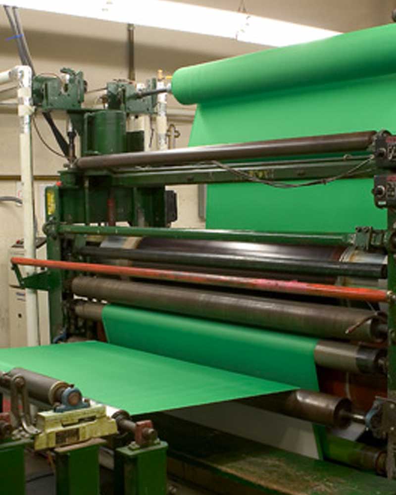 Green fabric going through rollers on a manufacturing machine